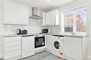 Een kleine keuken met witte kastjes, een inbouwoven, een magnetron en een vaatwasser.