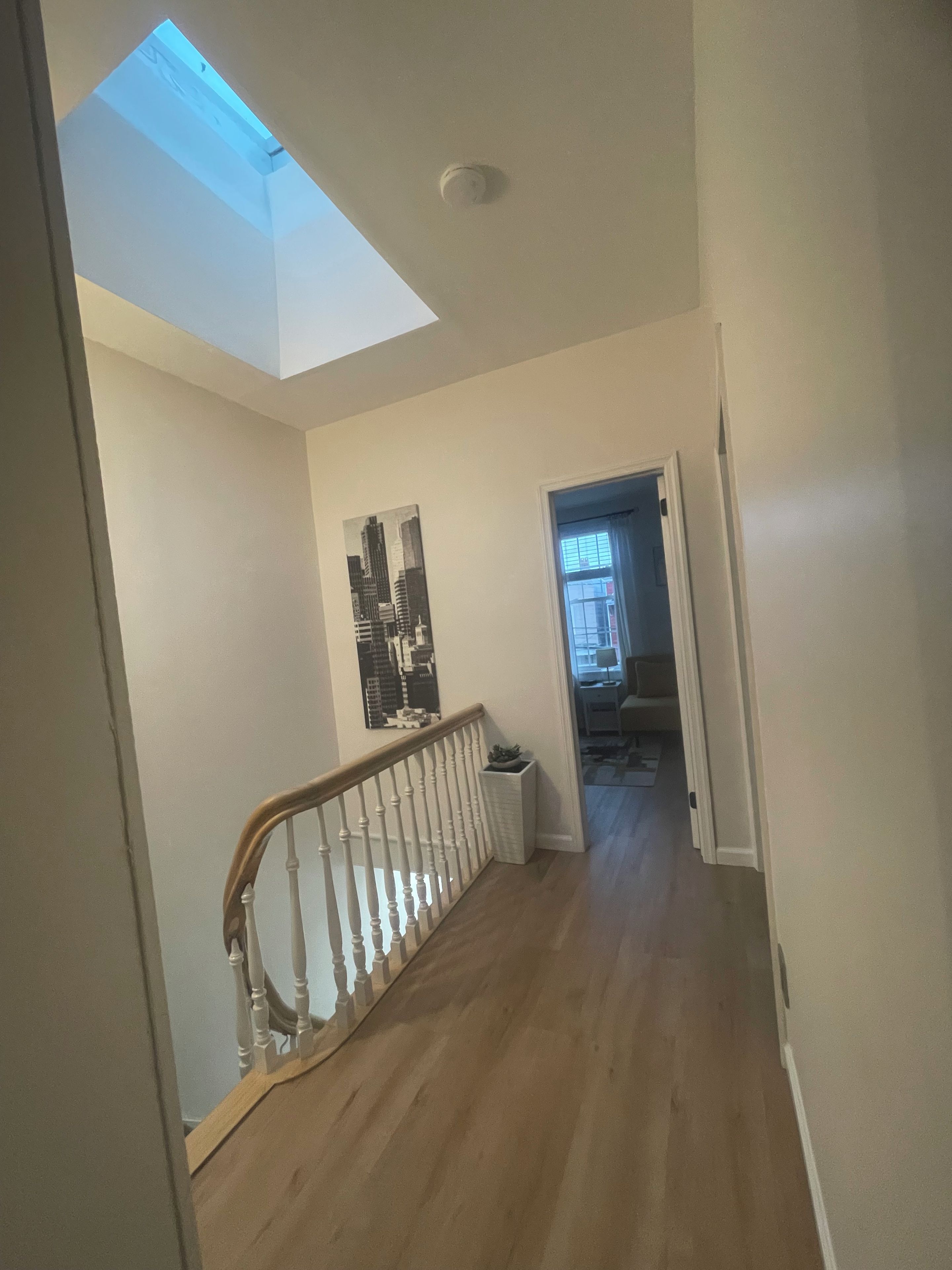 A hallway with a skylight, a staircase with a wooden railing, and a door leading to another room.