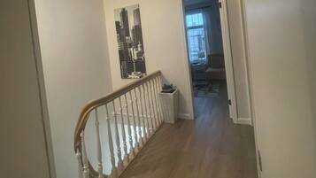 A hallway with a skylight, a staircase with a wooden railing, and a door leading to another room.