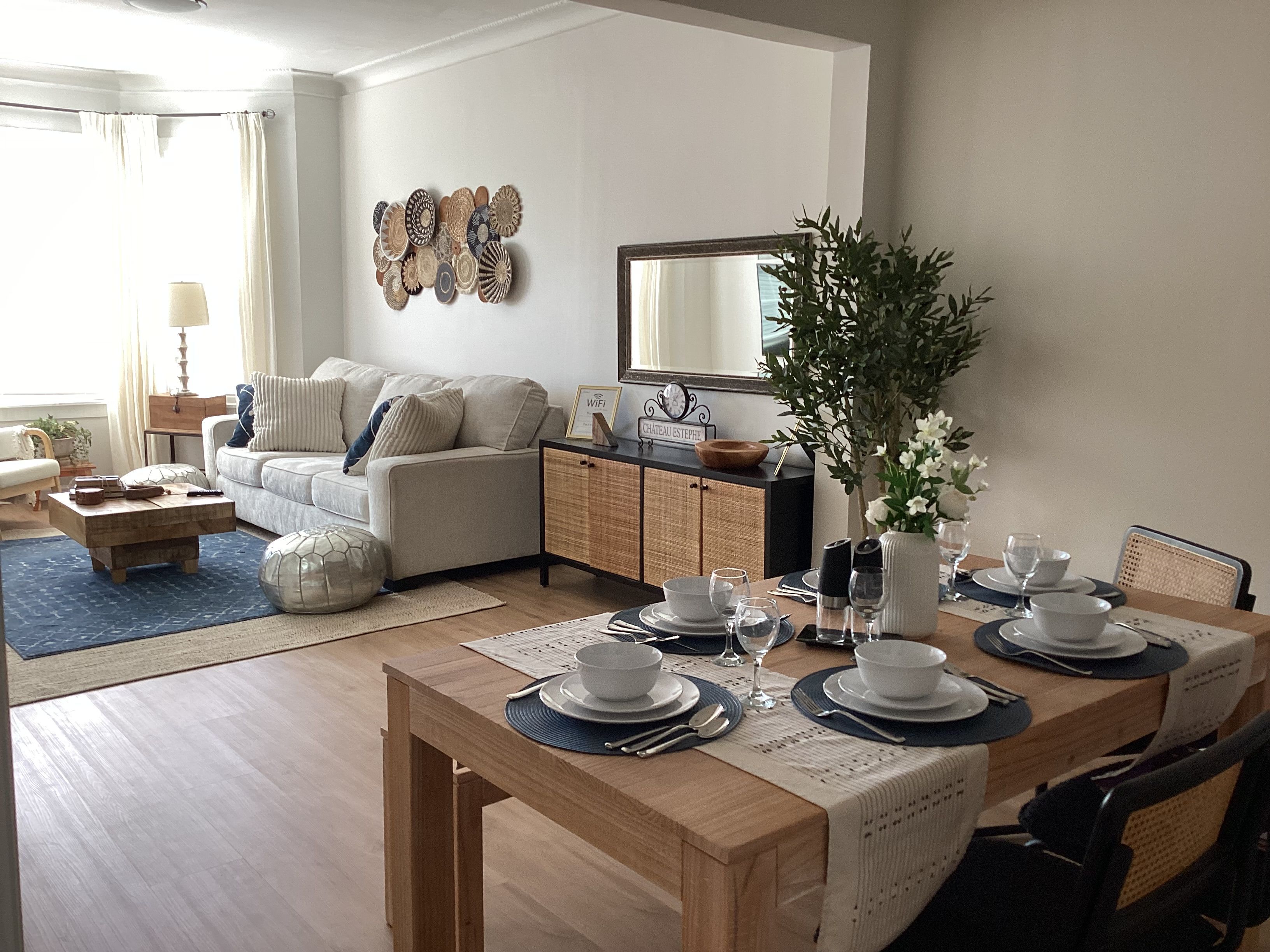 Uma sala de estar moderna com área de jantar, conjunto de sofás, mesa de centro e um painel decorativo na parede.