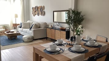 Uma sala de estar moderna com área de jantar, conjunto de sofás, mesa de centro e um painel decorativo na parede.