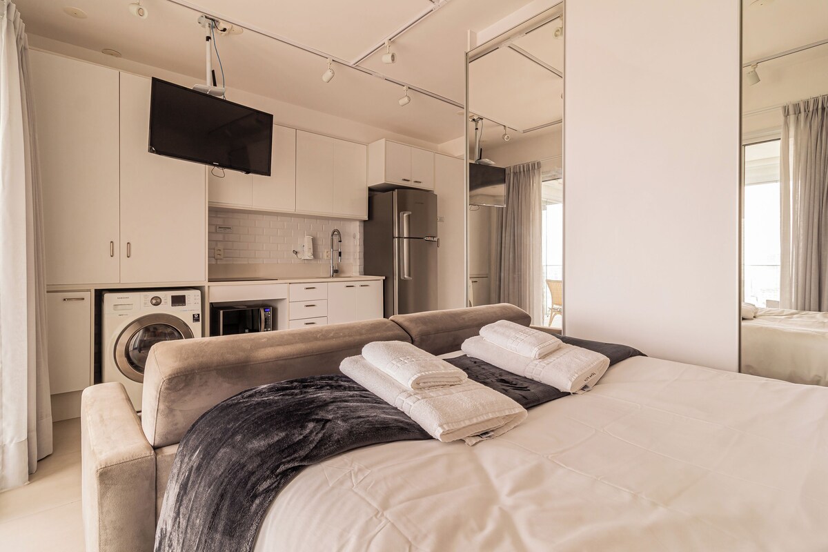 Ein modernes Schlafzimmer mit einem Bett, einem Flachbildfernseher, einer Waschmaschine, einem Kühlschrank und einer Küchenzeile.
