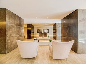 Ein modernes Interieur mit zwei weißen Sesseln, die sich einem zentralen Konsolentisch gegenüberstehen, einem Flachbildfernseher und einem großen abstrakten Gemälde an der Wand.