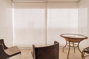 Ein Balkon mit Glastisch und -stühlen, Blick durch ein gemustertes Fenster und ein gefliester Boden.