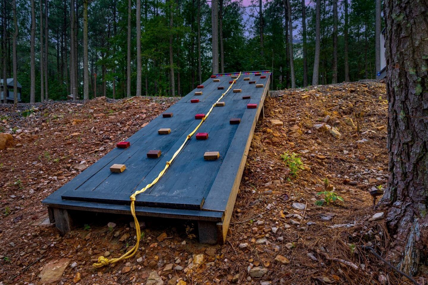A wooden ramp with red blocks and a yellow rope, surrounded by trees and a pile of leaves.