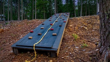 A wooden ramp with red blocks and a yellow rope, surrounded by trees and a pile of leaves.