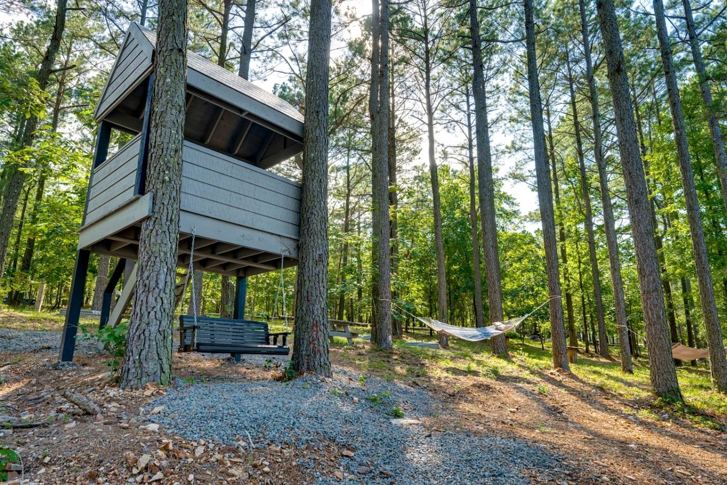 A treehouse with a bench and hammock in a forest.