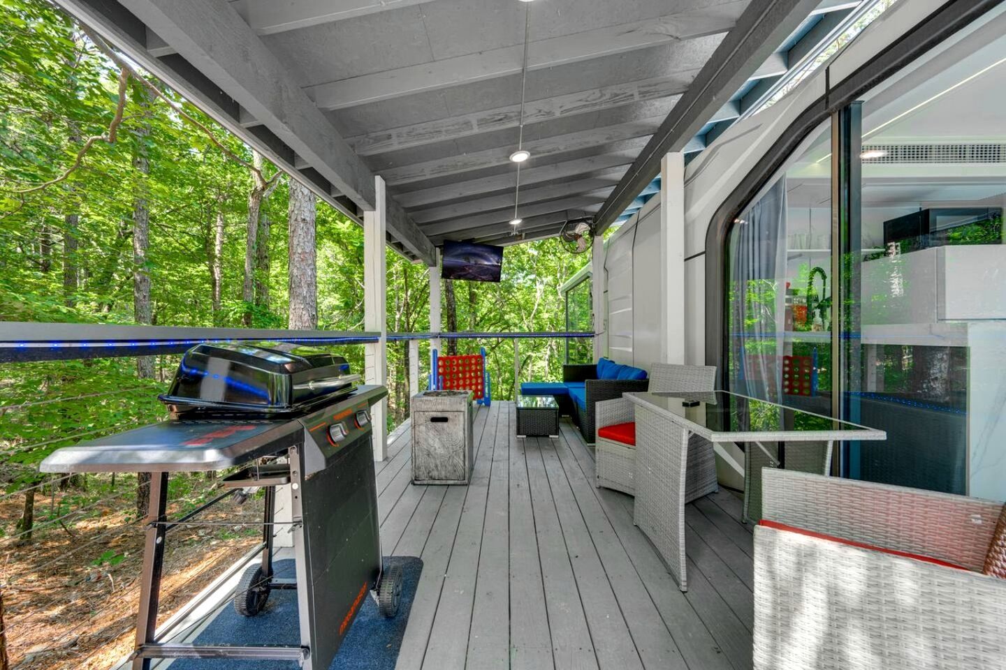 An outdoor deck with a grill, seating, and a glass enclosure with a view of greenery.