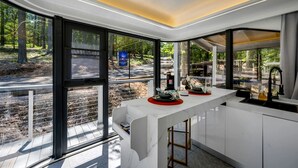 Una cocina moderna con amplios ventanales, encimera blanca y vistas a un área boscosa.