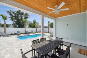 A covered outdoor area with a pool, lounge chairs, and a table. - Blissful Getaway (Panama City Beach)