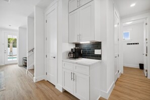 A modern kitchen with white cabinetry, a black tiled backsplash, and a coffee machine. - Blissful Getaway (Panama City Beach)