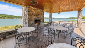 Une terrasse extérieure avec des murs en pierre, une cheminée et des meubles en métal, donnant sur un lac.