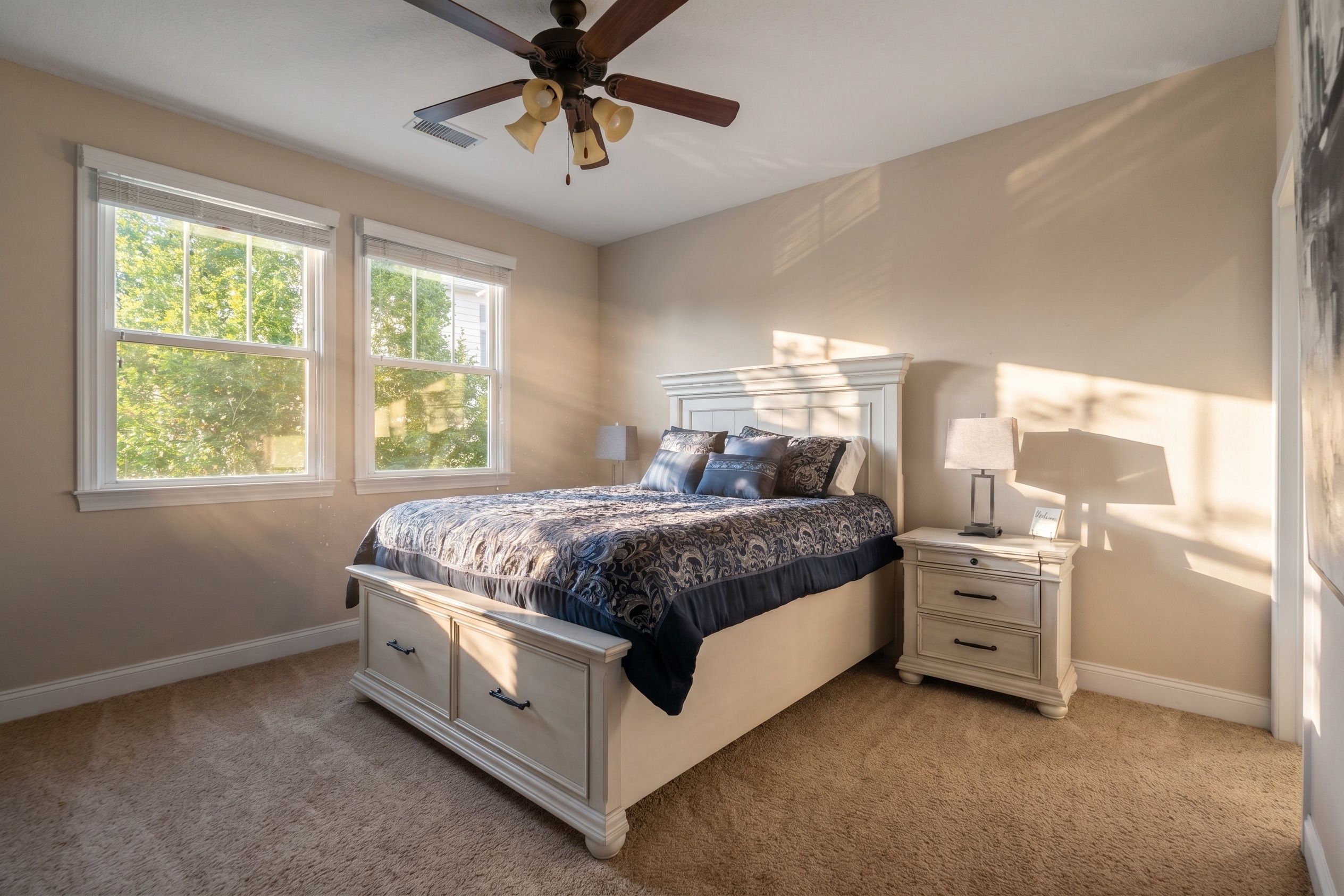 Une chambre à coucher avec un lit, des tables de chevet, un ventilateur de plafond et des fenêtres.