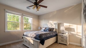 Une chambre à coucher avec un lit, des tables de chevet, un ventilateur de plafond et des fenêtres.