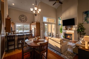 A spacious living area with a fireplace, a dining table with chairs, and a kitchen area with a large window.
