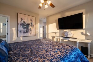 A bedroom with a large bed, a flat-screen TV mounted on the wall, and a ceiling fan.