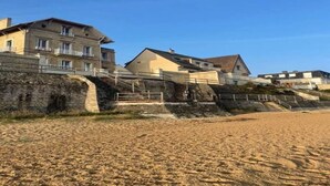 Ein Gebäude an der Küste mit mehreren Etagen, einer Steinsichtmauer und einem Sandstrand im Vordergrund.