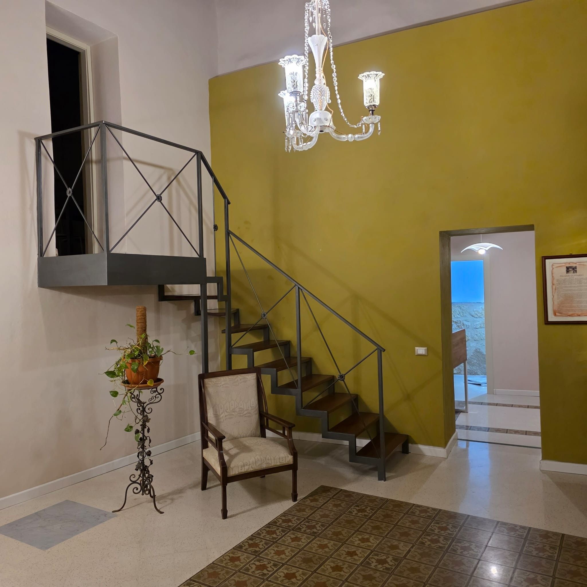 Una escalera con barandilla de metal, un candelabro, una silla y una planta en maceta.