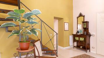 Una escalera con una planta en maceta, una silla, un mueble de madera con un espejo y una alfombra estampada.