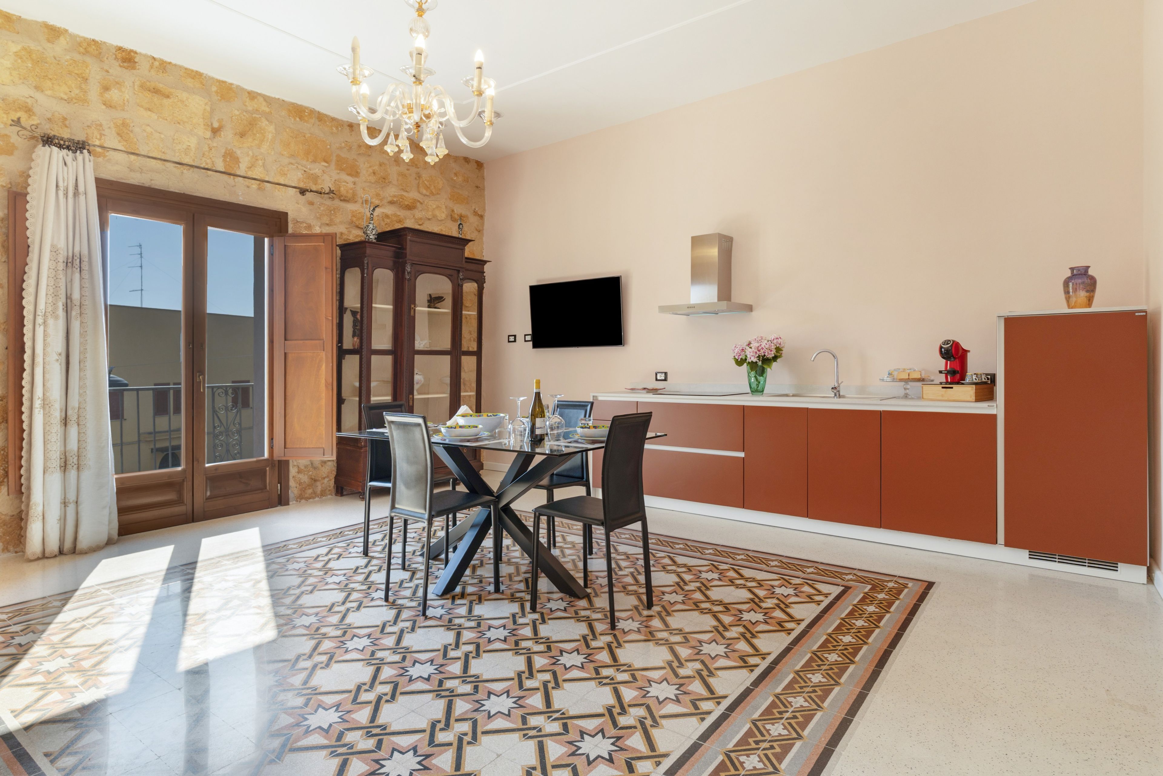 Zona pranzo con tavolo apparecchiato per quattro, un lampadario e una cucina con televisore a schermo piatto.