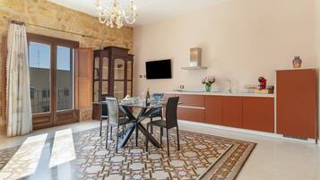 Zona pranzo con tavolo apparecchiato per quattro, un lampadario e una cucina con televisore a schermo piatto.