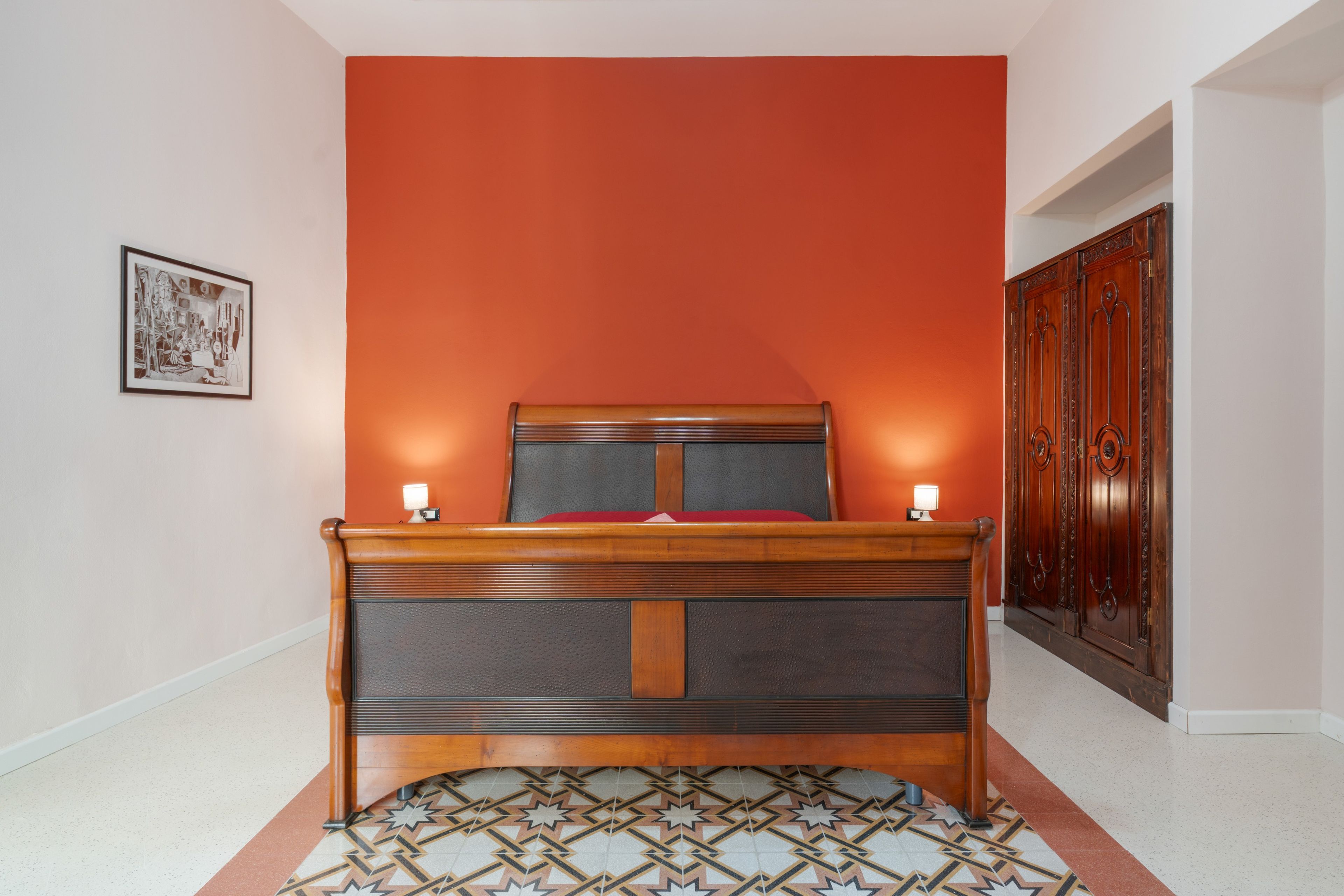 A bedroom with a wooden bed, a red headboard, a patterned rug, and a framed picture on the wall.