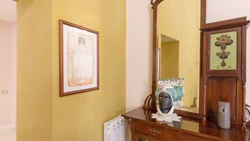 A room with a large mirror, a framed document on the wall, and a wooden cabinet with a decorative vase.