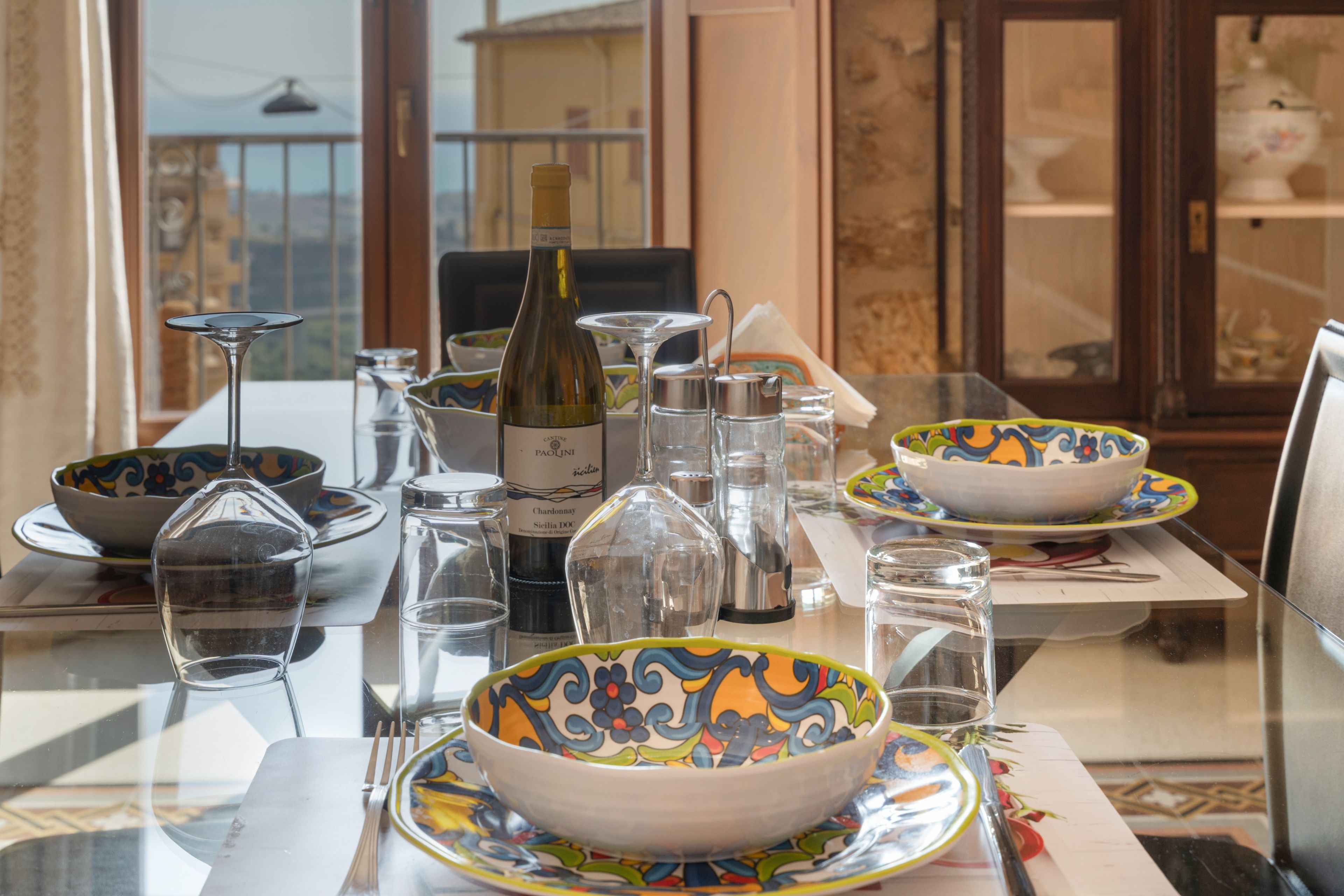 A dining table set with various glassware, a wine bottle, and colorful bowls.