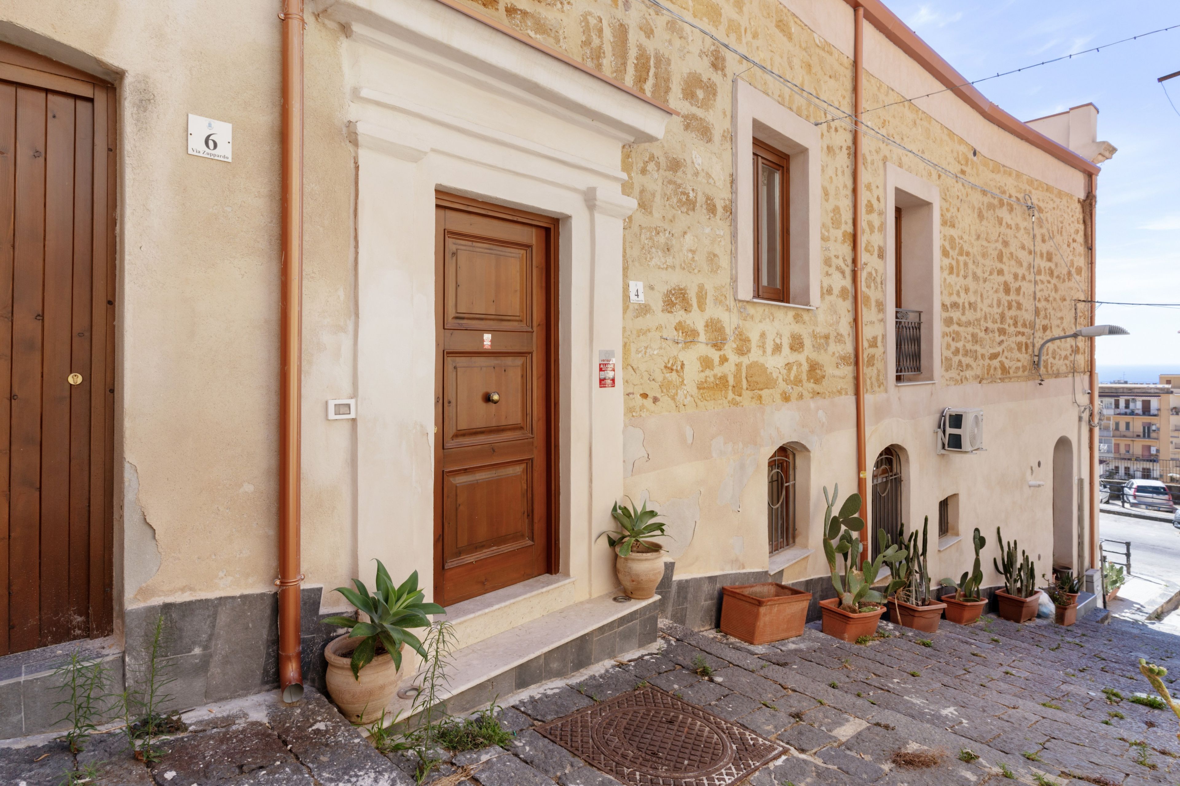 A building with a stone facade, wooden doors, and multiple potted plants on the ground.