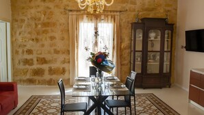 Un coin repas agrémenté d’un lustre, d’une table en verre, de chaises, d’un canapé rouge, d’un tapis à motifs et d’un meuble avec des portes en verre.