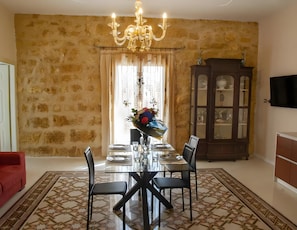 Ein Essbereich mit einer Chandelier, einem Glastisch, Stühlen, einem roten Sofa, einem gemusterten Teppich und einem Schrank mit Glastüren.