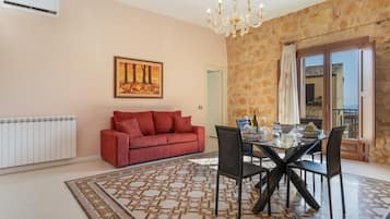 Zona pranzo con tavolo in vetro, sedie nere, tappeto decorato, divano rosso, un quadro e parete in pietra.