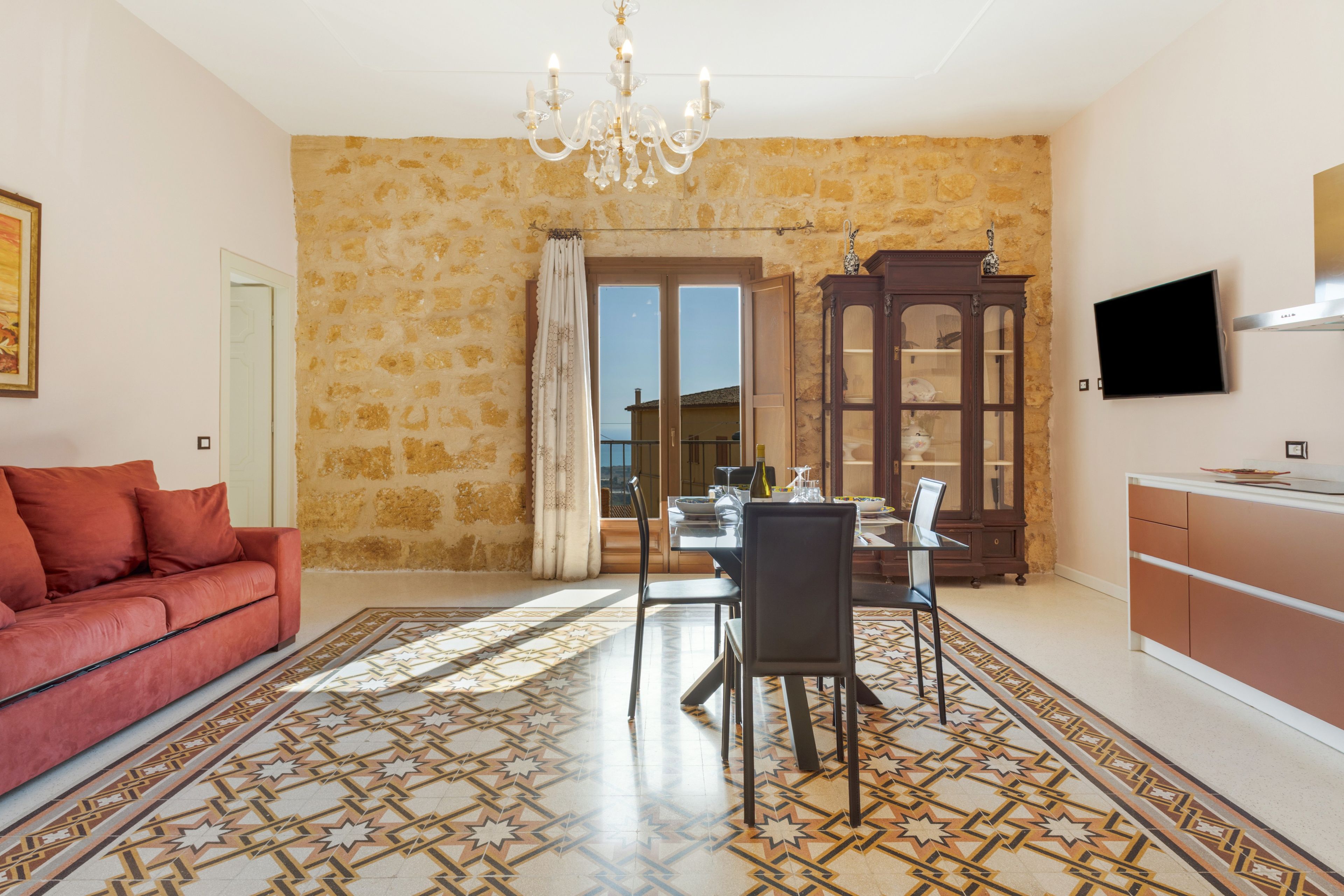 A dining area with a chandelier, a dining table with chairs, a cabinet, and a television mounted on the wall.