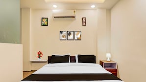 Habitación de hotel con cama, mesitas de noche, aire acondicionado instalado en la pared y cuadros enmarcados.