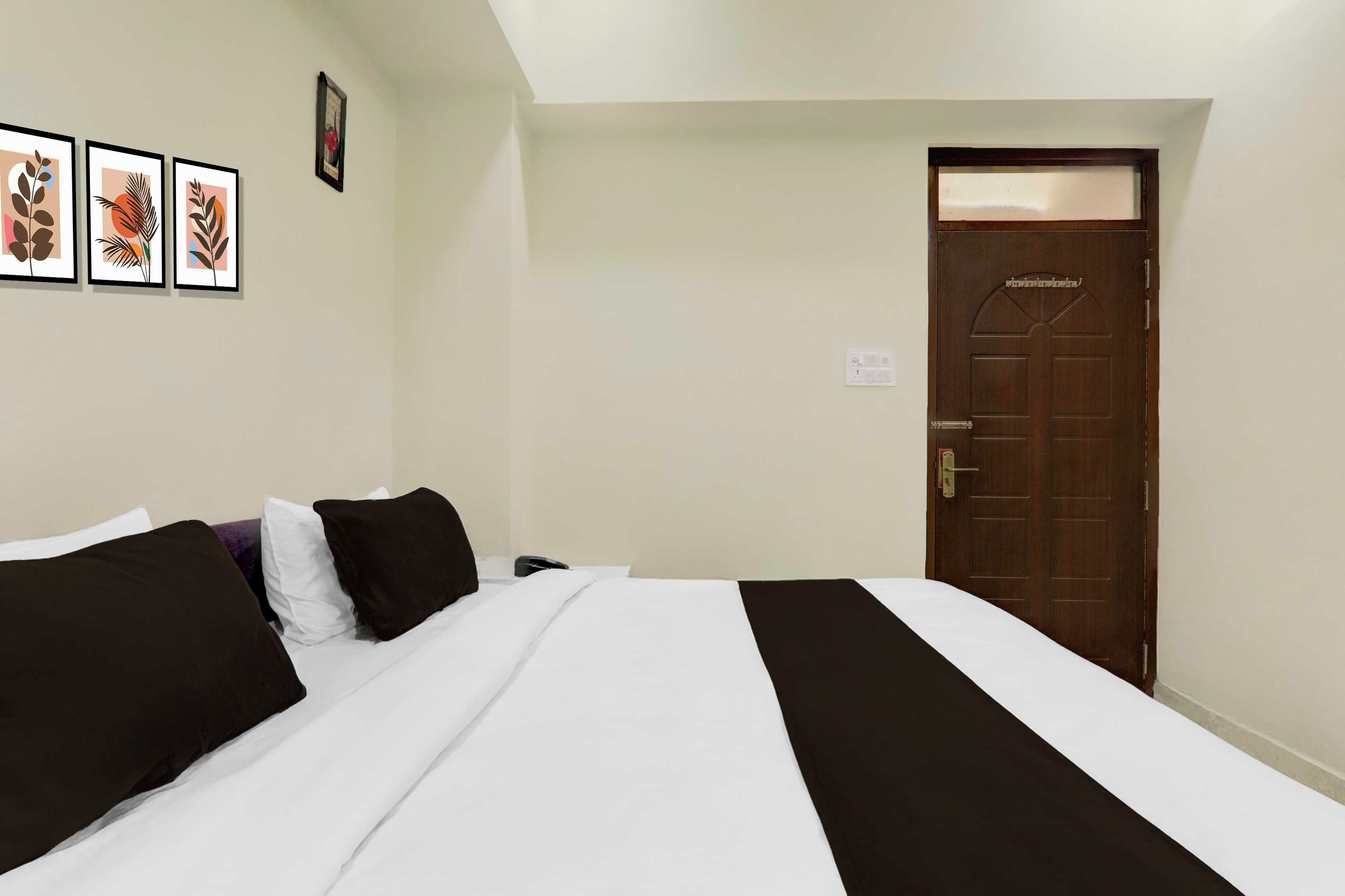 A hotel room with a bed, a door, and three framed pictures on the wall.