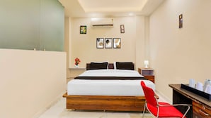 Una habitación de hotel con una cama, una silla roja, una mesita de noche, una lámpara y arte en la pared.