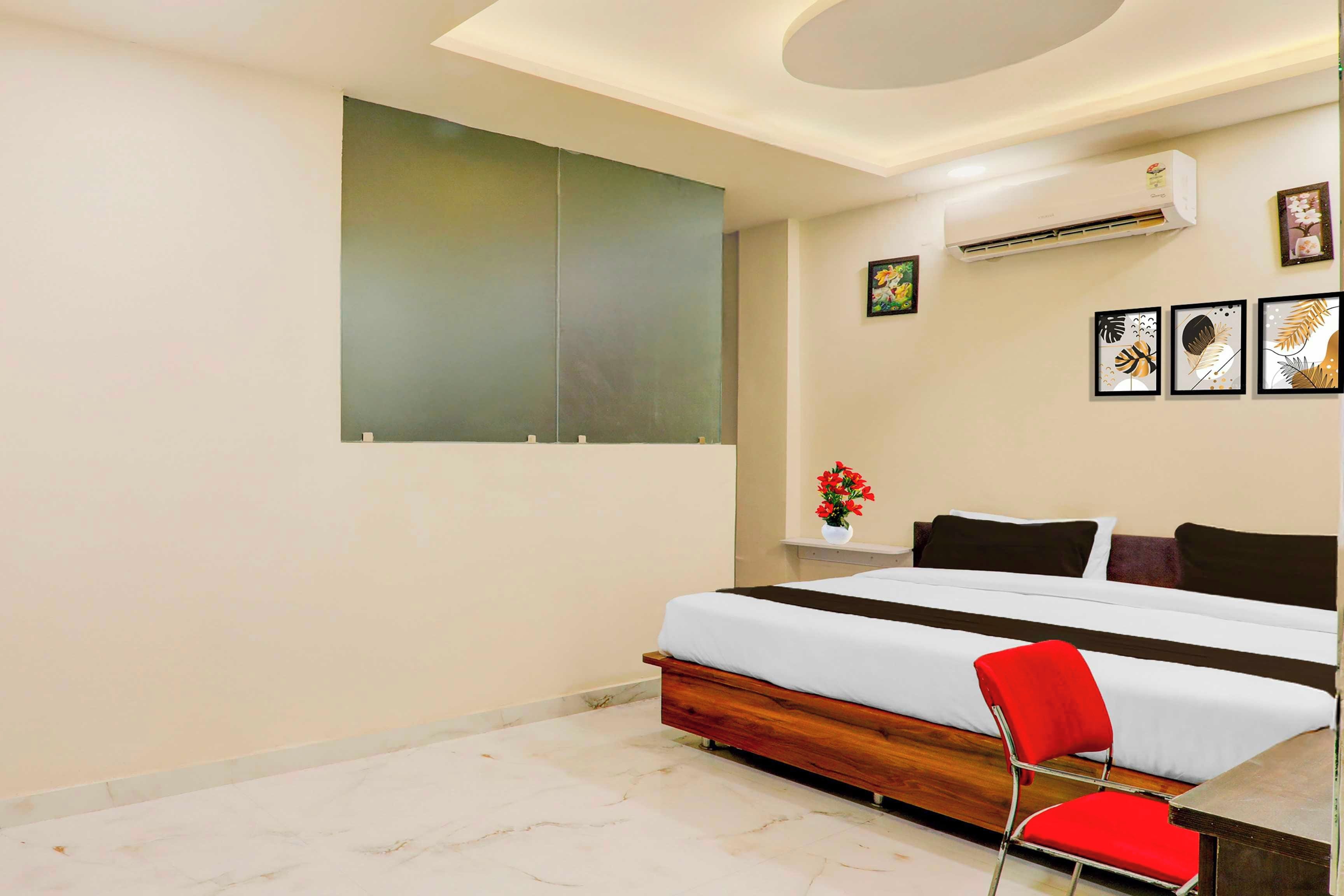 A hotel room with a bed, a red chair, a wall-mounted air conditioner, and artwork.