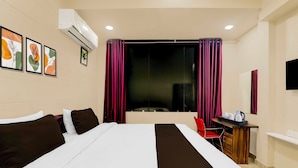 Una habitación de hotel con cama, escritorio, silla, televisor y obras de arte en la pared.