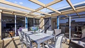 An outdoor patio with a glass enclosure, a table with chairs, and a grill area. - Beach Road Retreat  Pet Friendly Walk to Beach (Torquay)