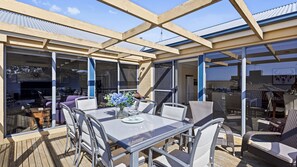 En udendørs terrasse med glasvægge, et bord med stole og et grillområde.