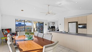 A modern kitchen with a built-in microwave, a dining area with a wooden table and white chairs, and a ceiling fan. - Beach Road Retreat  Pet Friendly Walk to Beach (Torquay)