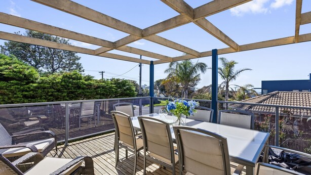 An outdoor patio with a table and chairs, surrounded by a wooden deck and glass railing. - Beach Road Retreat  Pet Friendly Walk to Beach (Torquay)