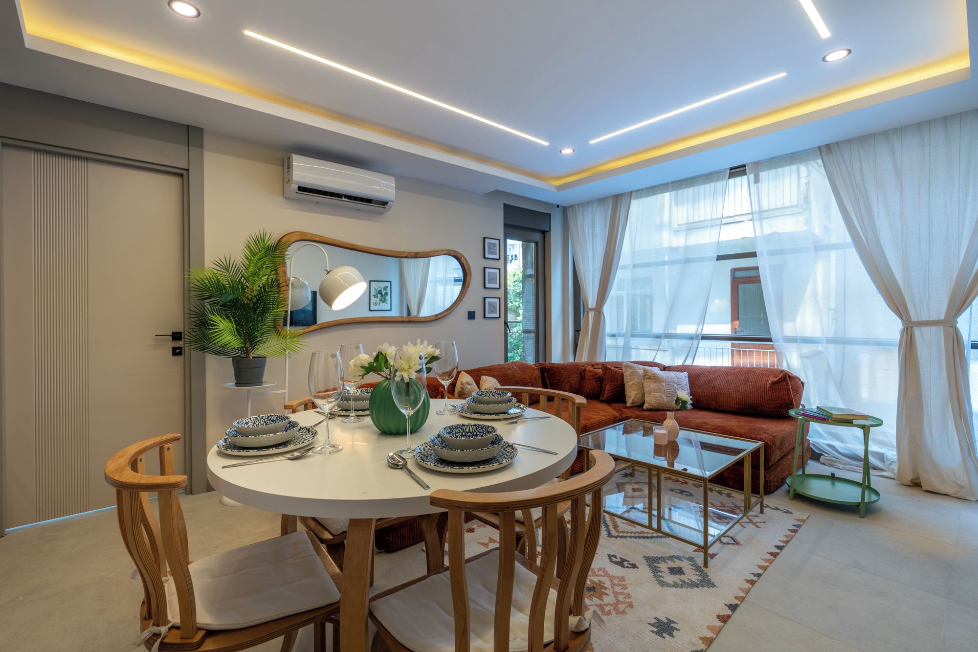 Een moderne woonkamer met een ronde eettafel, houten stoelen, een bank en een glazen salontafel.
