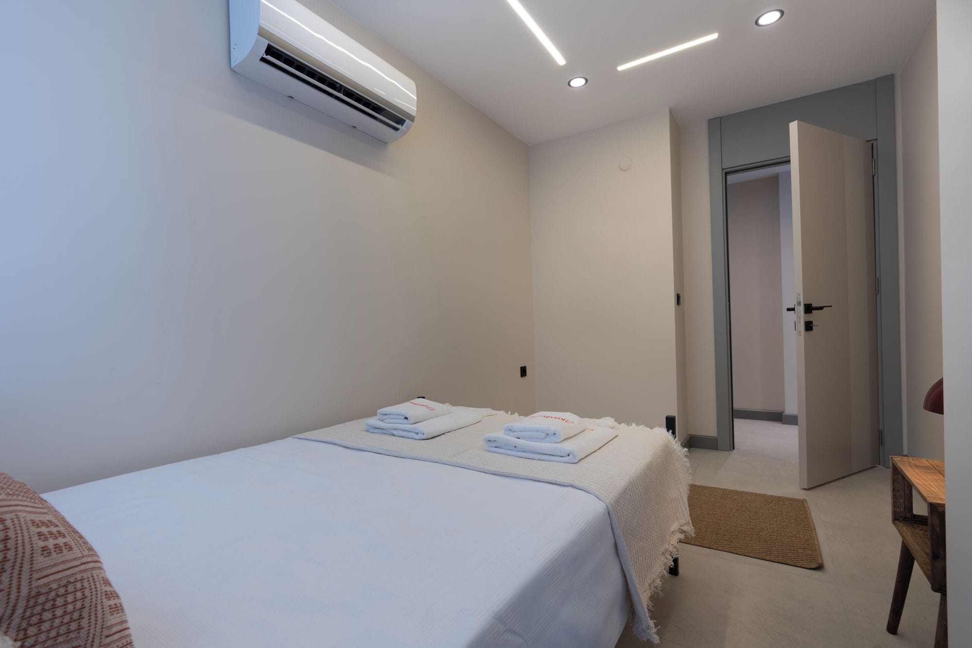 A hotel room with a bed, a wall-mounted air conditioner, a door, and a small wooden table.