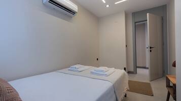 A hotel room with a bed, a wall-mounted air conditioner, a door, and a small wooden table.