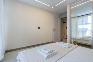 A hotel room with a bed, a bedside table, a mirror, and a door leading to another room.