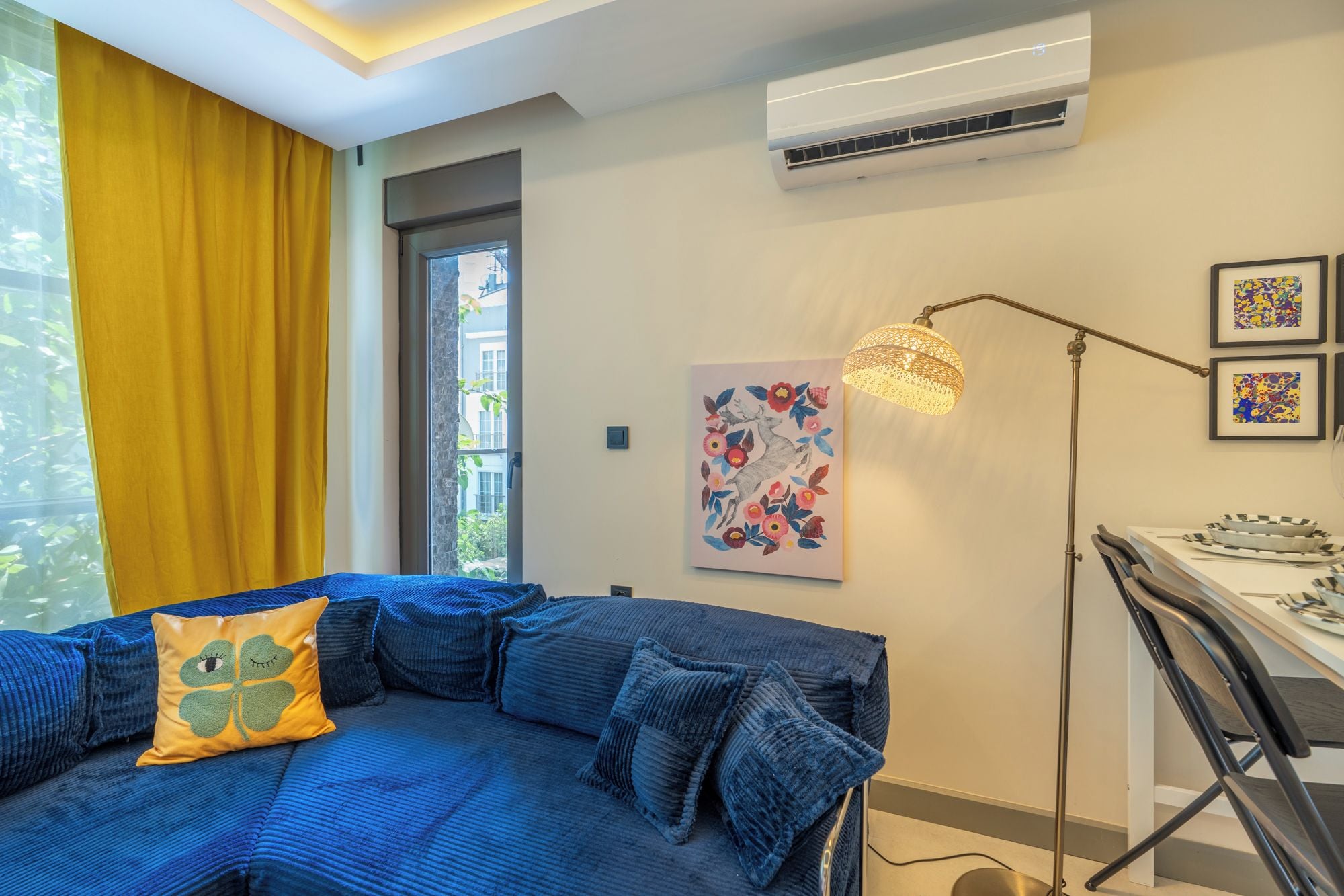 A modern room with a blue sofa, a yellow curtain, an air conditioning unit, and a floor lamp.