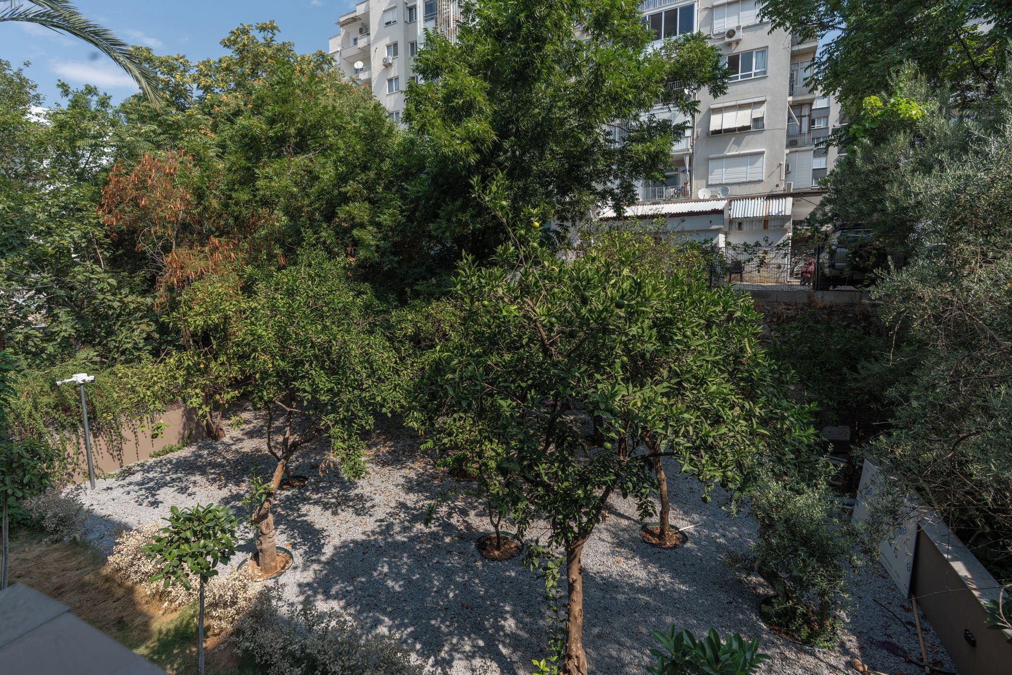 A residential area with multiple apartment buildings, trees, and a gravel pathway.