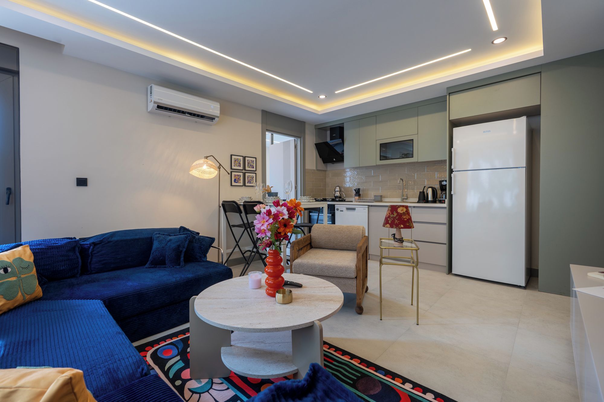 Een moderne woonkamer met een bank, een salontafel en een eethoek met stoelen en een lamp.