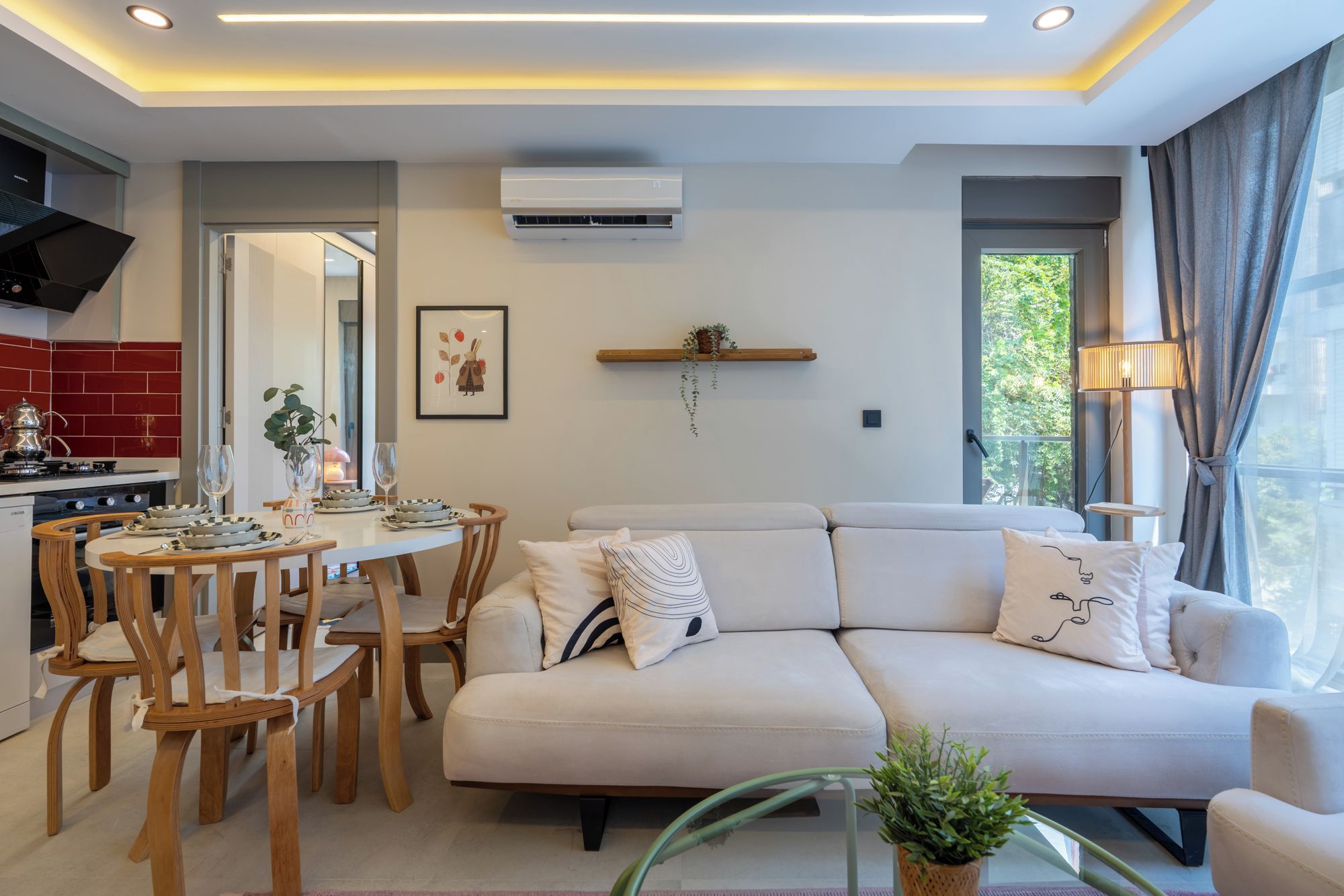 A modern living room with a sofa, dining table, chairs, and a kitchen area with a stove.